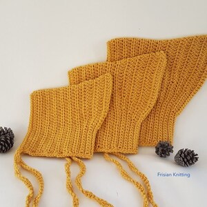 Op de afbeelding: Drie gele gehaakte baby mutsjes met bandjes, in een rij op een wit oppervlak gerangschikt. De mutsjes zijn gemaakt met een eenvoudig steekpatroon en hebben een puntige vorm. De mutsjes zijn een populaire keuze voor baby's en peuters.