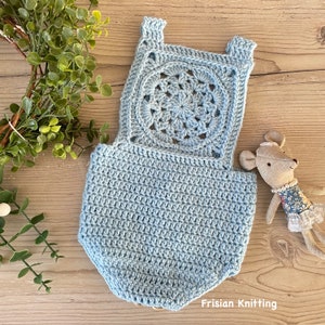 May include: A light blue crocheted baby romper with a large circular design on the back. The romper is made with a delicate stitch and has a scalloped edge.