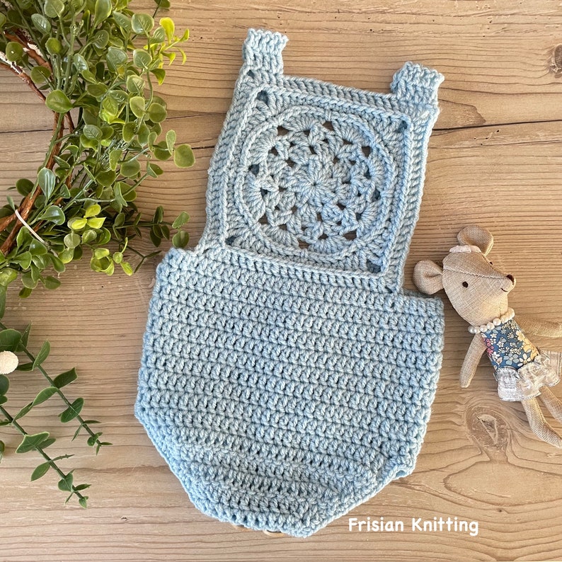 May include: A light blue crocheted baby romper with a large circular design on the back. The romper is made with a delicate stitch and has a scalloped edge.