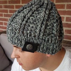 Op de afbeelding: Een grijze en witte gebreide beanie met een zwart leren patch waarop "Sun Rise" staat.