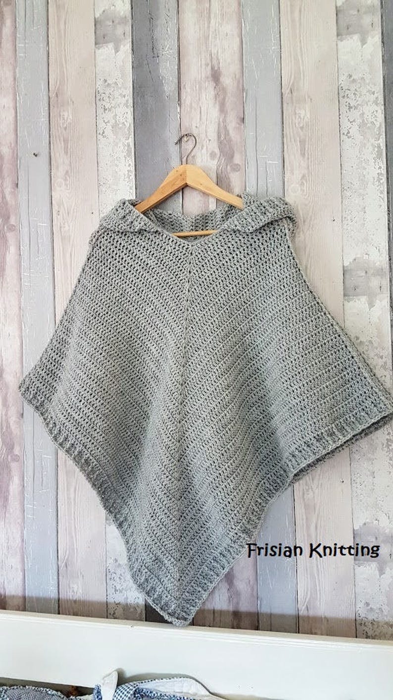 K&ouml;nnte beinhalten: Ein graues H&auml;kelponcho mit Kapuze, das an einem Holzb&uuml;gel an einer Holzvert&auml;felung h&auml;ngt. Der Text "Frisian Knitting" ist in der rechten unteren Ecke des Bildes sichtbar.