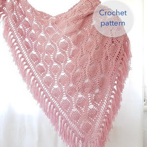 Può includere: Uno scialle rosa all'uncinetto con un delicato motivo a pizzo e frange. Lo scialle è drappeggiato su un manichino e il testo "Crochet pattern" è visibile nell'immagine.