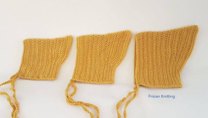 Op de afbeelding: Drie gele gehaakte baby mutsjes met bandjes. De mutsjes zijn in verschillende maten, met het grootste mutsje rechts en het kleinste mutsje links.
