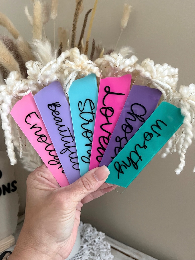 Puede incluir: Seis marcadores de libros acr&iacute;licos de colores con caligraf&iacute;a negra. Los marcadores dicen "enough", "beautiful", "strong", "loved", "wisdom", y "dream".
