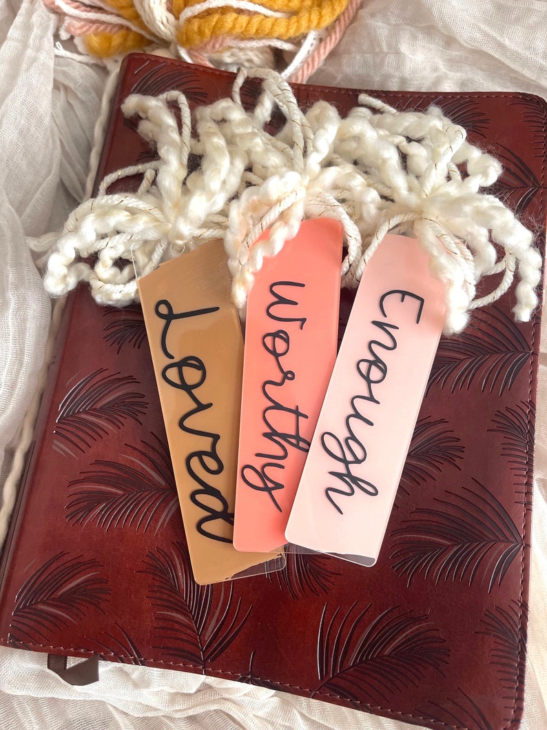 Puede incluir: Tres marcap&aacute;ginas con las palabras "Loved", "Worthy" y "Enough" escritas en letra negra sobre un diario de cuero marr&oacute;n con un patr&oacute;n de hojas de palma.