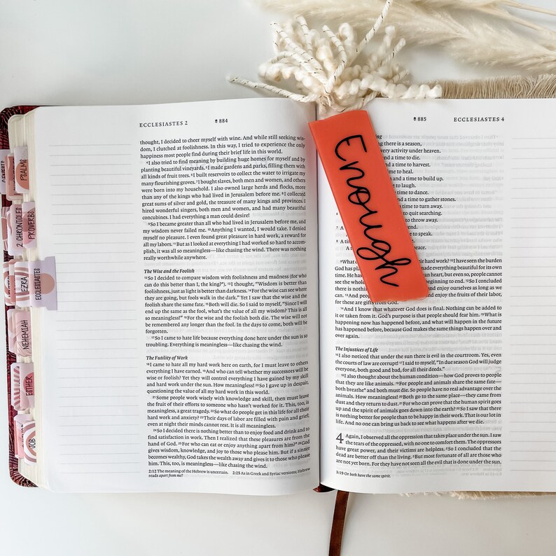 Puede incluir: Primer plano de un marcap&aacute;ginas rojo con la palabra "Enough" escrita en letras negras. El marcap&aacute;ginas est&aacute; colocado en una Biblia abierta con el texto "Eclesiast&eacute;s 4" visible en la p&aacute;gina.