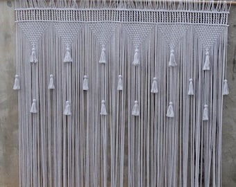 May include: A white macrame wall hanging with a geometric pattern and tassels. The hanging is made of cotton cord and is approximately 90 cm wide and 150 cm tall.