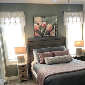May include: A bedroom with a gray bed frame, a pink and gray quilt, and a framed print of a cactus with pink flowers. The room has a gray rug, a white nightstand, and a white lamp.