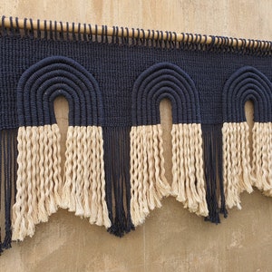 May include: A wall hanging with three black and white macrame rainbows. The rainbows are made with thick rope and have a fringe at the bottom.