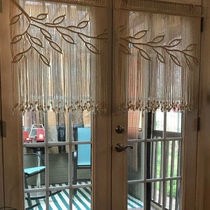 Può includere: Tende in macramè bianche con un motivo a foglie appese a un set di porte francesi che conducono a un patio con due sedie e un tappeto a strisce.