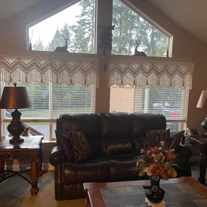 K&ouml;nnte beinhalten: Ein Wohnzimmer mit einem braunen Ledersofa, zwei Beistelltischen mit Lampen und einem Couchtisch mit einer Blumenvase. Die Fenster haben wei&szlig;e H&auml;kelvorh&auml;nge und Jalousien.