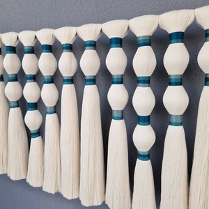 May include: A wall hanging made of white yarn with blue and teal ribbon accents. The yarn is tied into a series of knots and then fanned out to create a cascading effect.