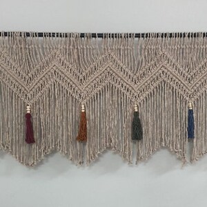 May include: A beige macrame wall hanging with a chevron pattern and tassels in various colors, including blue, green, red, and orange.