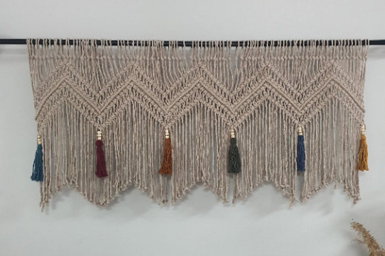 May include: A beige macrame wall hanging with a chevron pattern and tassels in various colors, including blue, green, red, and orange.