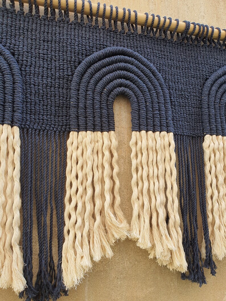 May include: A wall hanging with a woven design of two arches in navy blue with a fringe of cream colored yarn.
