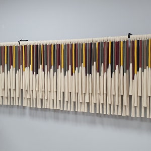 May include: A wall hanging made of yarn with tassels. The yarn is in shades of red, yellow, green, and brown. The tassels are white.