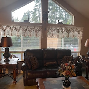 K&ouml;nnte beinhalten: Ein Wohnzimmer mit einem braunen Ledersofa, zwei Beistelltischen mit Lampen und einem Couchtisch mit einer Blumenvase. Die Fenster haben wei&szlig;e H&auml;kelvorh&auml;nge und Jalousien.