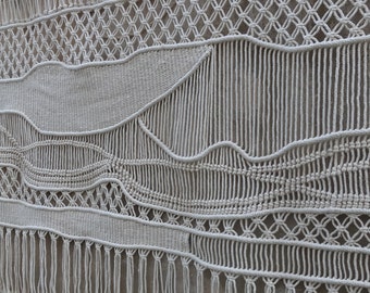 May include: A white macrame wall hanging with a geometric design and fringe. The hanging is made of natural cotton rope and has a rustic, bohemian style.
