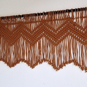 May include: A brown macrame wall hanging with a chevron pattern and fringe.