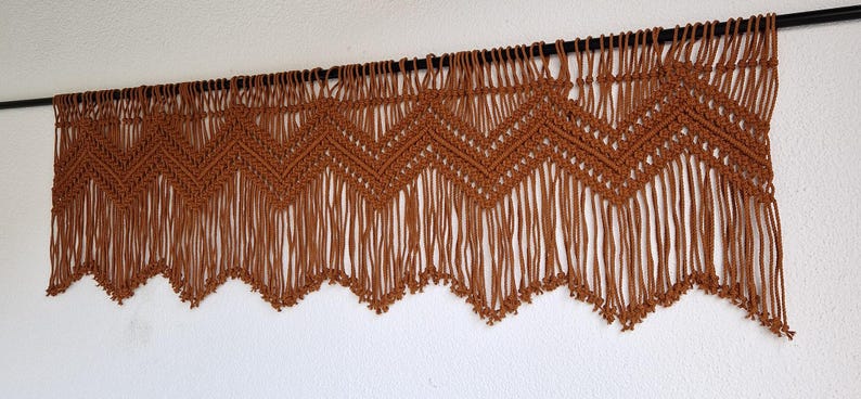 May include: A brown macrame wall hanging with a chevron pattern and fringe.