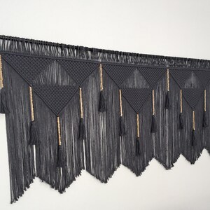 May include: A gray macrame wall hanging with wooden beads and tassels. The hanging is made of a thick, textured yarn and has a geometric pattern.