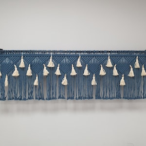 May include: A blue macrame wall hanging with white tassels. The hanging is made of cotton cord and has a geometric pattern.