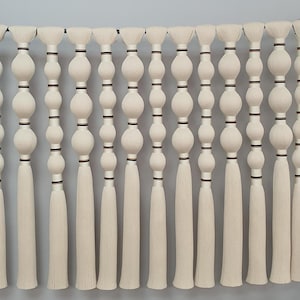 May include: A wall hanging made of white yarn with black accents. The hanging features a series of knotted balls and tassels.