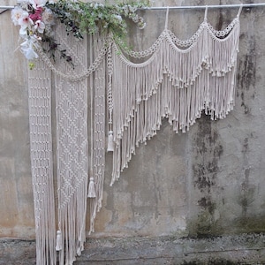 May include: A white macrame wall hanging with a variety of textures and patterns. The hanging is made of cotton cord and features a fringe design.