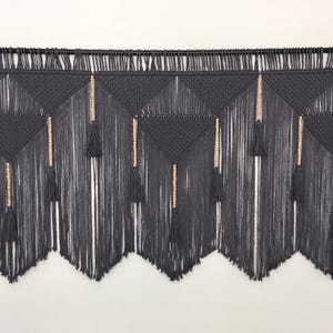 May include: Gray macrame wall hanging with wooden beads and tassels. The wall hanging is made of a thick, textured cord and has a geometric pattern.