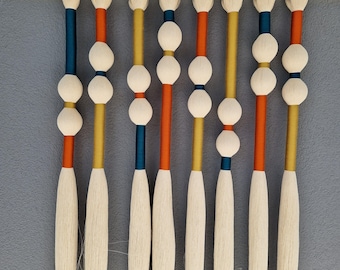 May include: A decorative wall hanging with multiple vertical strands. Each strand has a white tassel, white spherical beads, and sections of teal, orange, and yellow. The strands are suspended from a black horizontal line, creating a colourful display.