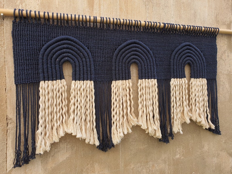 May include: A wall hanging with three black and white macrame rainbows. The rainbows are made with thick rope and have a fringe at the bottom.