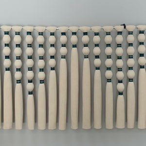 May include: A wall hanging made of white yarn with teal and white beads. The yarn is hanging in strands from a metal rod.