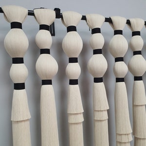 May include: A set of six white macrame wall hangings with black trim. Each hanging has three tiers of fringe and a series of black bands.