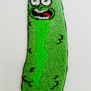 May include: Green embroidered patch of a pickle character with a wide open mouth and a tongue sticking out. The pickle has a light blue headband and black eyes.