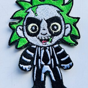 May include: An embroidered iron-on patch featuring a cartoon character with green hair, a black and white striped suit, and a white face with black eyes and a green mouth.