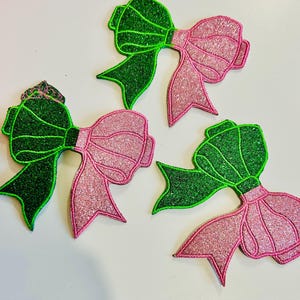May include: Three green and pink glitter bows. The bows are made of felt and have a sparkly finish.