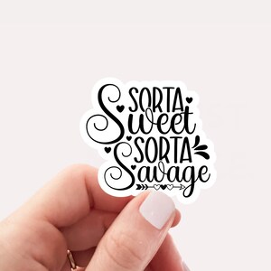 May include: A white sticker with the text "Sorta Sweet Sorta Savage" in black script. The sticker is held by a hand against a white background. The design includes hearts and arrows.
