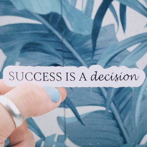 May include: White sticker with the text "SUCCESS IS A decision" on a blue and white tropical leaf background.