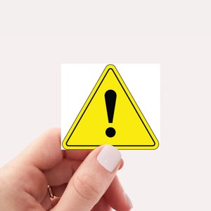 May include: A yellow triangle warning sign with a black exclamation point in the center. The sign is being held by a hand.