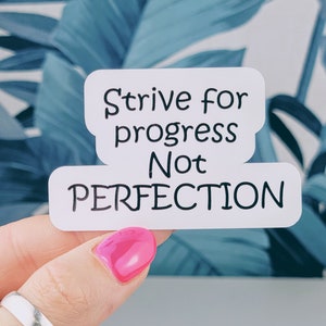 May include: White sticker with black text that reads "Strive for progress Not Perfection". A hand is holding the sticker against a blue and white background.