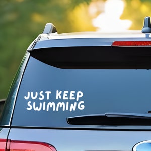 May include: A white vinyl sticker with the text "JUST KEEP SWIMMING" on a black car.