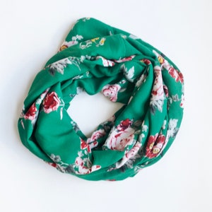 May include: A green infinity scarf with a floral print featuring pink, red, and white roses.