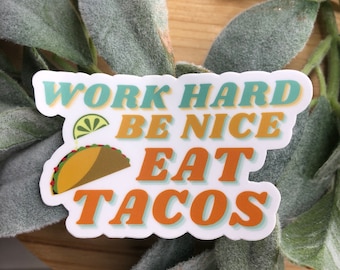 May include: A white sticker with the text "Work Hard Be Nice Eat Tacos" in a retro font. The text is in shades of blue, yellow, and orange. A cartoon taco with a lime wedge is pictured next to the text.
