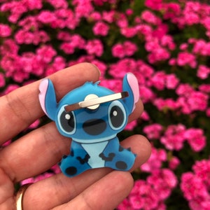 May include: Blue Stitch phone ring holder with a silver swivel ring. The Stitch character is sitting with its arms crossed and has a big smile.