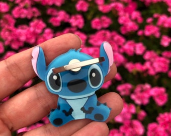 May include: Blue Stitch phone ring holder with a silver swivel ring. The Stitch character is sitting with its arms crossed and has a big smile.