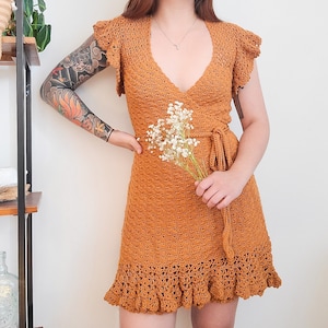 May include: A mustard yellow crochet dress with a V-neckline and a wrap-style bodice. The dress has a ruffled hem and is made of a lightweight, breathable fabric.