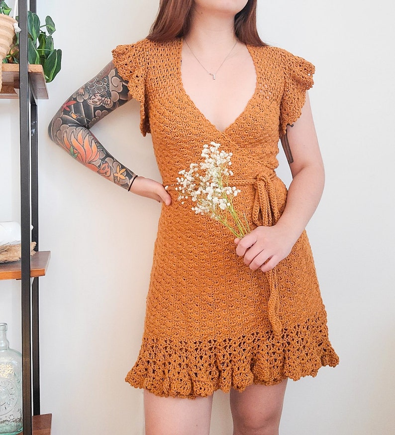 May include: A mustard yellow crochet dress with a V-neckline and a wrap-style bodice. The dress has a ruffled hem and is made of a lightweight, breathable fabric.