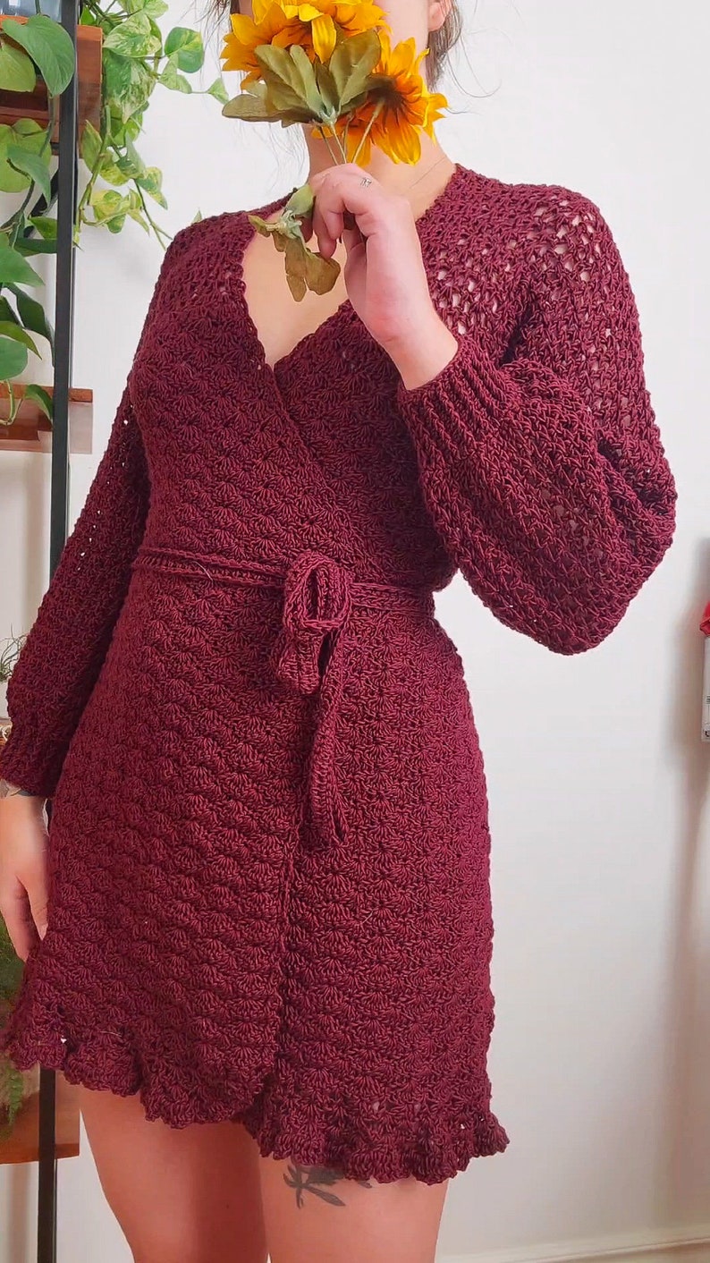 May include: A maroon crocheted wrap dress with long sleeves and a tie belt. The dress has a ruffled hem and a delicate openwork pattern.