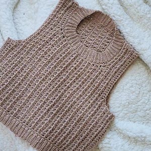 May include: A sleeveless crocheted top in a light brown colour. The top has a round neckline and a ribbed texture.