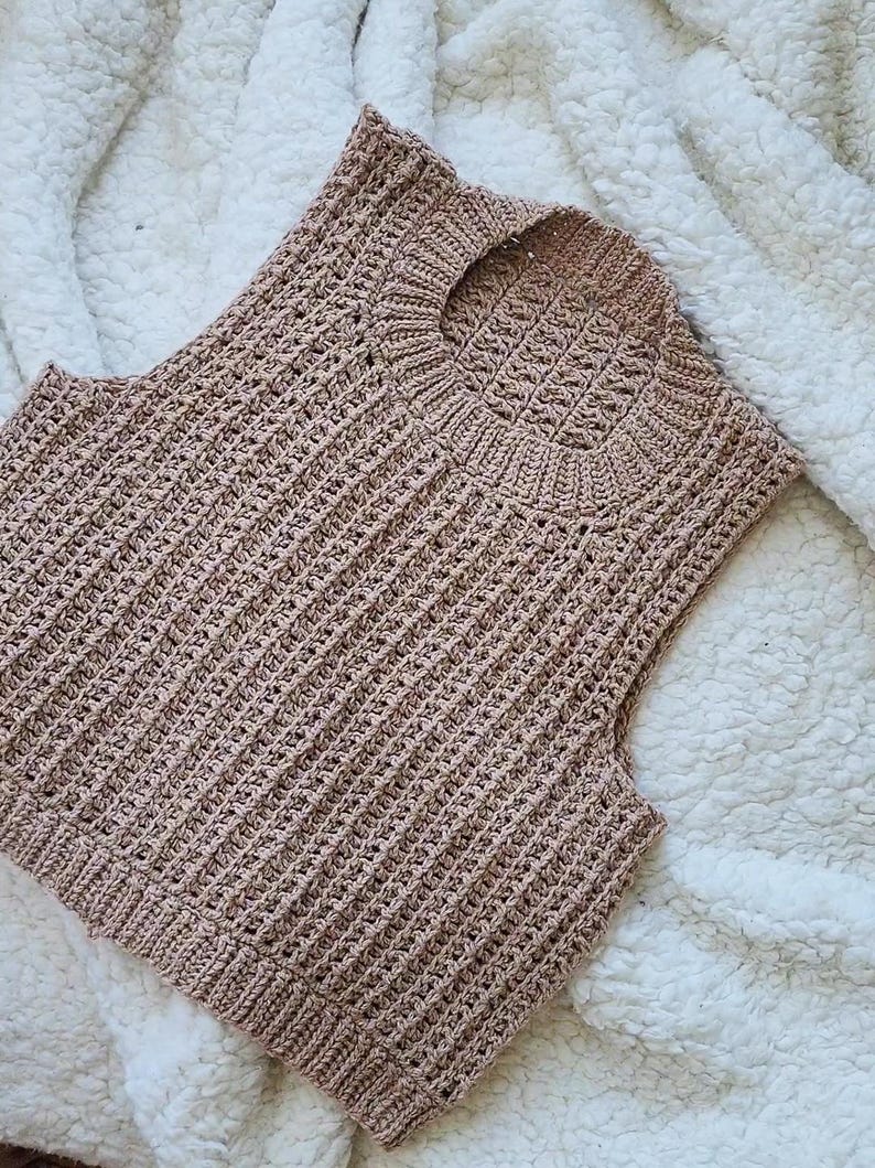 May include: A sleeveless crocheted top in a light brown colour. The top has a round neckline and a ribbed texture.
